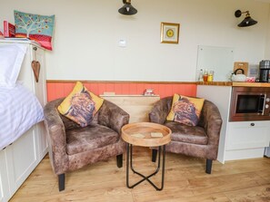 A cozy room with two brown leather sofas, a small wooden table, a kitchen area with a stove, and a white cabinet. - The Herdsman, Barnoldswick (Barnoldswick)