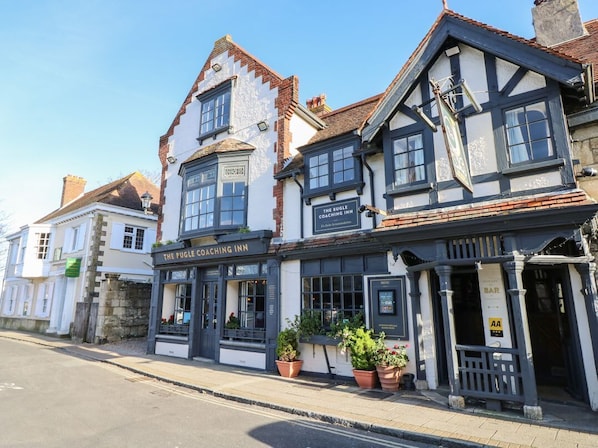 A traditional pub with a sign reading 'The Puggle Coaching Inn,' featuring a classic Tudor-style architecture with a prominent gabled roof and a visible entrance.