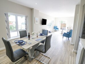 A modern dining area with a long table, chairs, and a television mounted on the wall. - Charming Southend Home in Welland (Malvern)
