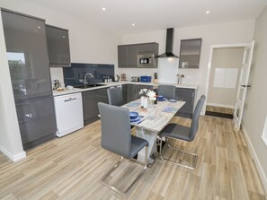 A modern kitchen with grey cabinets, a white countertop, and a dining table set for four. - Charming Southend Home in Welland (Malvern)
