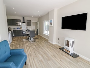 A modern living room with a flat-screen TV, a blue sofa, and a kitchen in the background. - Charming Southend Home in Welland (Malvern)