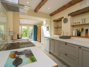 A modern kitchen with a central island, wooden beams, and a view to the outside.