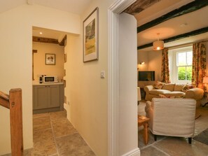 A hallway leading to a kitchen with a microwave and cabinets, a living room with a sofa and curtains, and a wooden staircase.