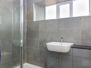 Ein Badezimmer mit Duschkabine aus Glas, einem weißen Waschbecken und einem dunklen Schrank.