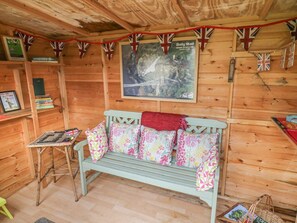 A wooden cabin interior with a bench, shelves with books, a framed picture, and a red banner.