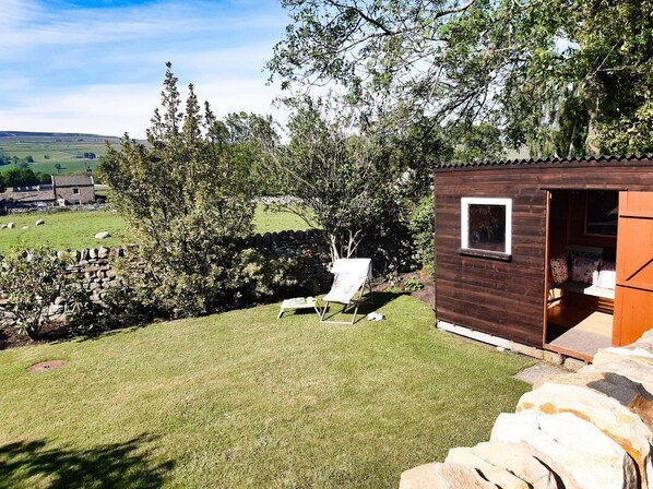 A wooden cabin with a small porch, a grassy yard, and a stone wall.
