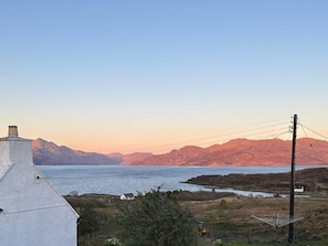 A coastal landscape with mountains, a body of water, and a white building with a chimney. - Charming Solas in Scenic Broadford (Isle of Skye)