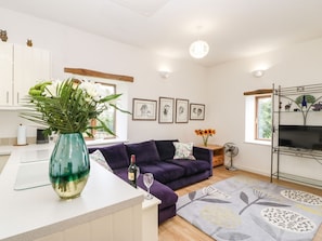 A modern living space with a sofa, a vase with flowers, a wine bottle, and framed artwork on the wall. - Whinstone in The Lake District (Appleby-in-Westmorland)