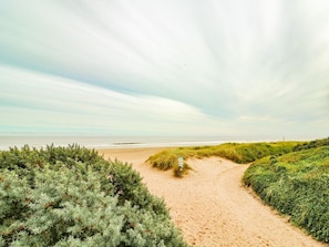 A sandy beach path with grassy dunes, a signpost, and the ocean in the background. - Windyridge, Chapel St Leonards (Skegness)