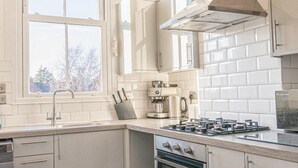 Une cuisine moderne avec des meubles blancs, un four encastré, une cuisinière et une fenêtre qui laisse entrer la lumière naturelle.