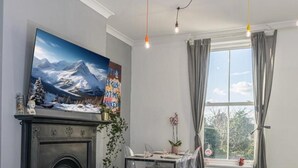 Un salon moderne avec une cheminée, une table à manger avec des chaises, une grande fenêtre avec des rideaux et un tableau accroché au mur.