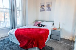 Une chambre à coucher avec un lit, des oreillers, une table de chevet, une lampe et une fenêtre.