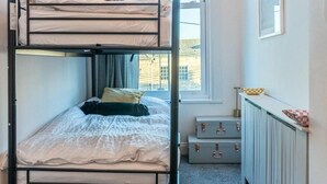 Une chambre avec un lit superposé, une fenêtre, un radiateur et un bureau.