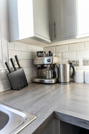 Une cuisine équipée d’une machine à café, d’une bouilloire et d’un bloc à couteaux.