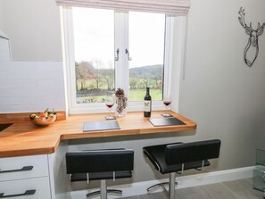 A kitchen with a wooden countertop, two black bar stools, a window with a view of a landscape, and a decorative deer head on the wall. - Roughwood, Poulner, Hampshire (Ringwood)