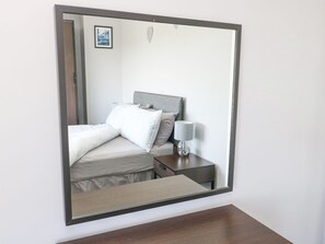 A bedroom with a bed, bedside table, lamp, and a mirror on the wall. - Pentre Iago Rhoscolyn Anglesey (Holyhead)