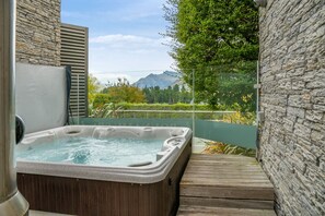 Un bain à remous avec vue sur les montagnes, entouré de murs en pierre et d’une terrasse en bois.