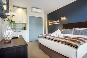 Une chambre d’hôtel avec un lit, un bureau, un vase de fleurs, un tableau et une porte donnant sur une salle de bain.