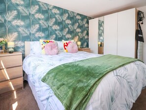 A bedroom with a bed, a green throw blanket, and a wall with a leaf pattern.