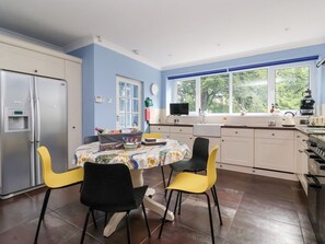 Een keuken met een eettafel, stoelen, een koelkast en een raam met uitzicht op groen.