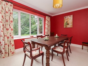 Een eetkamer met een houten tafel en stoelen, rode muren en een raam met gordijnen.