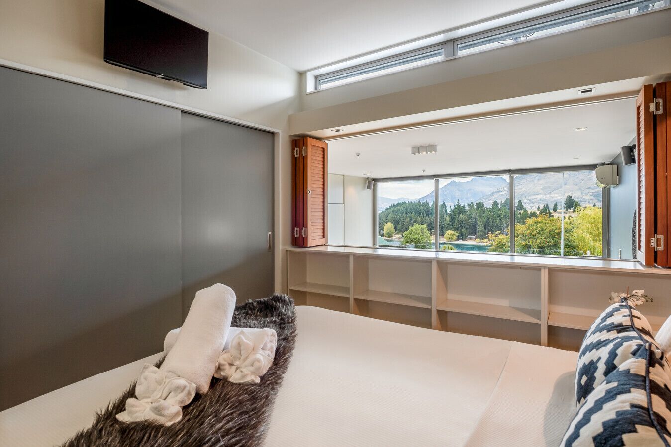 Een slaapkamer met een groot raam, een flatscreen-tv en een bont vloerkleed.