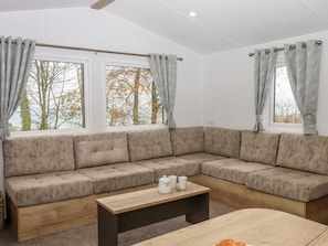 A modern living room with a sectional sofa, a wooden coffee table, and large windows with curtains.