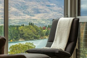 Une chaise recouverte d’une serviette blanche, placée près d’une fenêtre donnant sur un lac et des collines boisées.