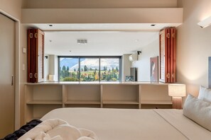 Une chambre avec un grand lit, une fenêtre donnant sur les montagnes, un bureau avec une lampe et une armoire.