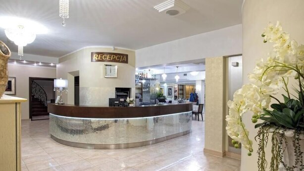 A reception area with a reception desk, a staircase, and a wall-mounted sign. - Hotel Lord Krosno (Krosno)