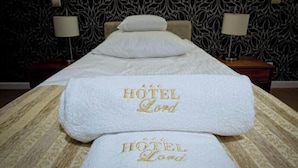 A hotel room with a massage table, two towels with 'HOTEL Lord' embroidered, and patterned wallpaper. - Hotel Lord Krosno (Krosno)