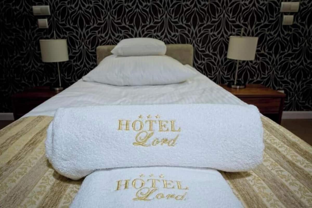 A hotel room with a massage table, two towels with 'HOTEL Lord' embroidered, and patterned wallpaper.