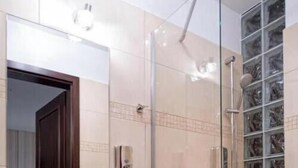 A bathroom with a glass-enclosed shower, a sink, and a tiled wall. - Hotel Lord Krosno (Krosno)