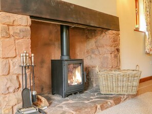 A stone fireplace with a black wood-burning stove, a metal stand with candles, and a wicker basket.