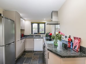 A modern kitchen with a dishwasher, stainless steel refrigerator, and a window with a view of the backyard.