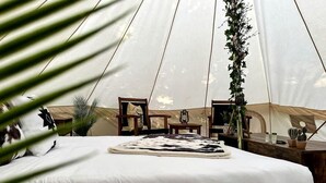 A tented accommodation with a bed, wooden furniture, and potted plants.