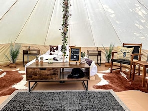 A tent interior with a wooden table, potted plants, a sign, and a cowhide rug.