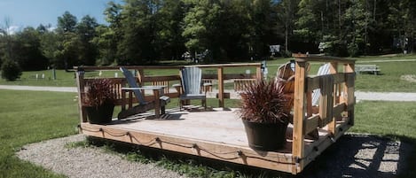 Een houten terras met tuinmeubilair, omgeven door een grindpad en begroeiing.
