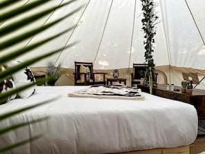 Een tentaccomodatie met een bed, houten meubels en potplanten.