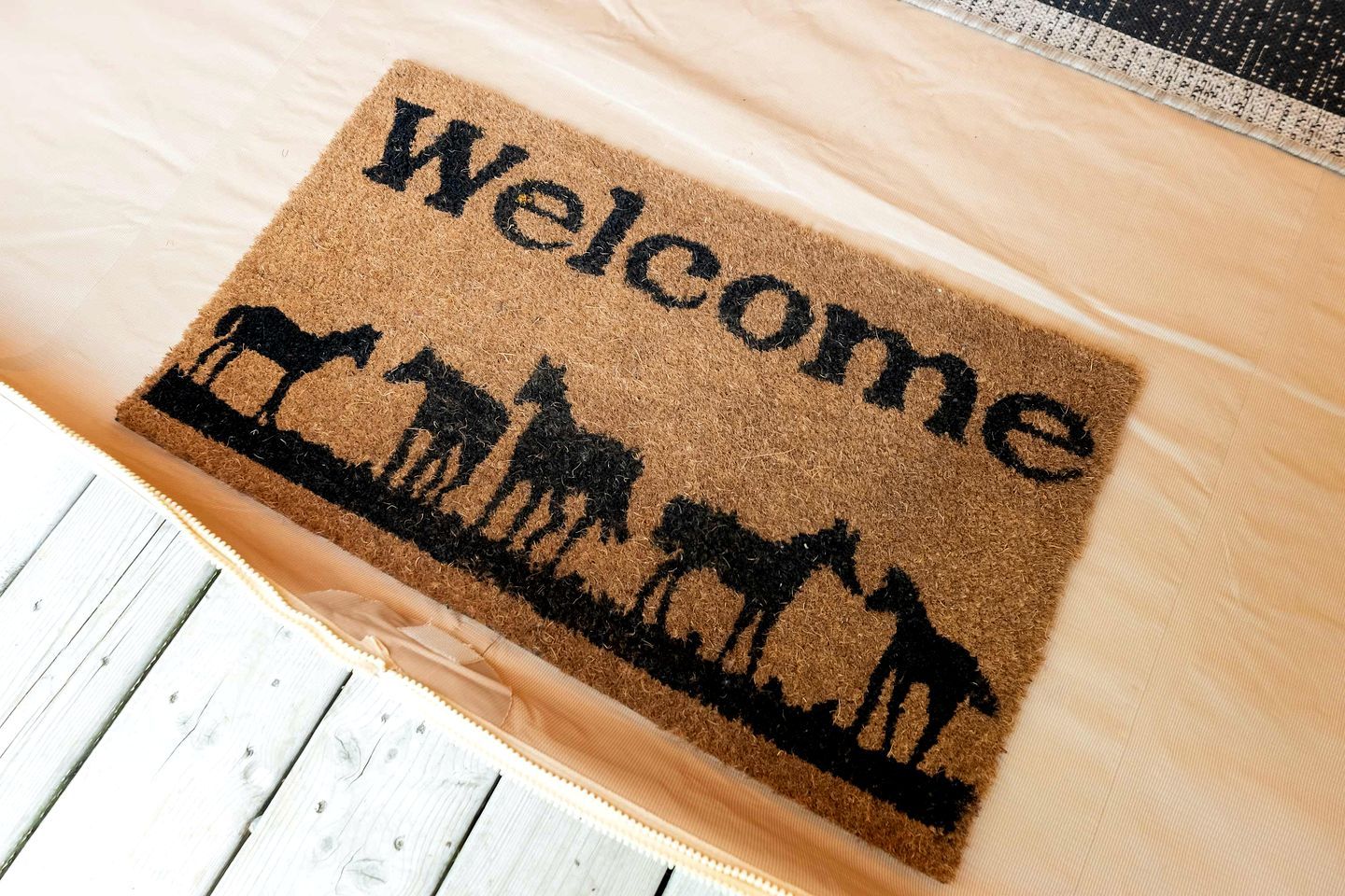 Alfombra de bienvenida con la silueta de un caballo y la palabra 'Welcome' sobre un piso de madera.