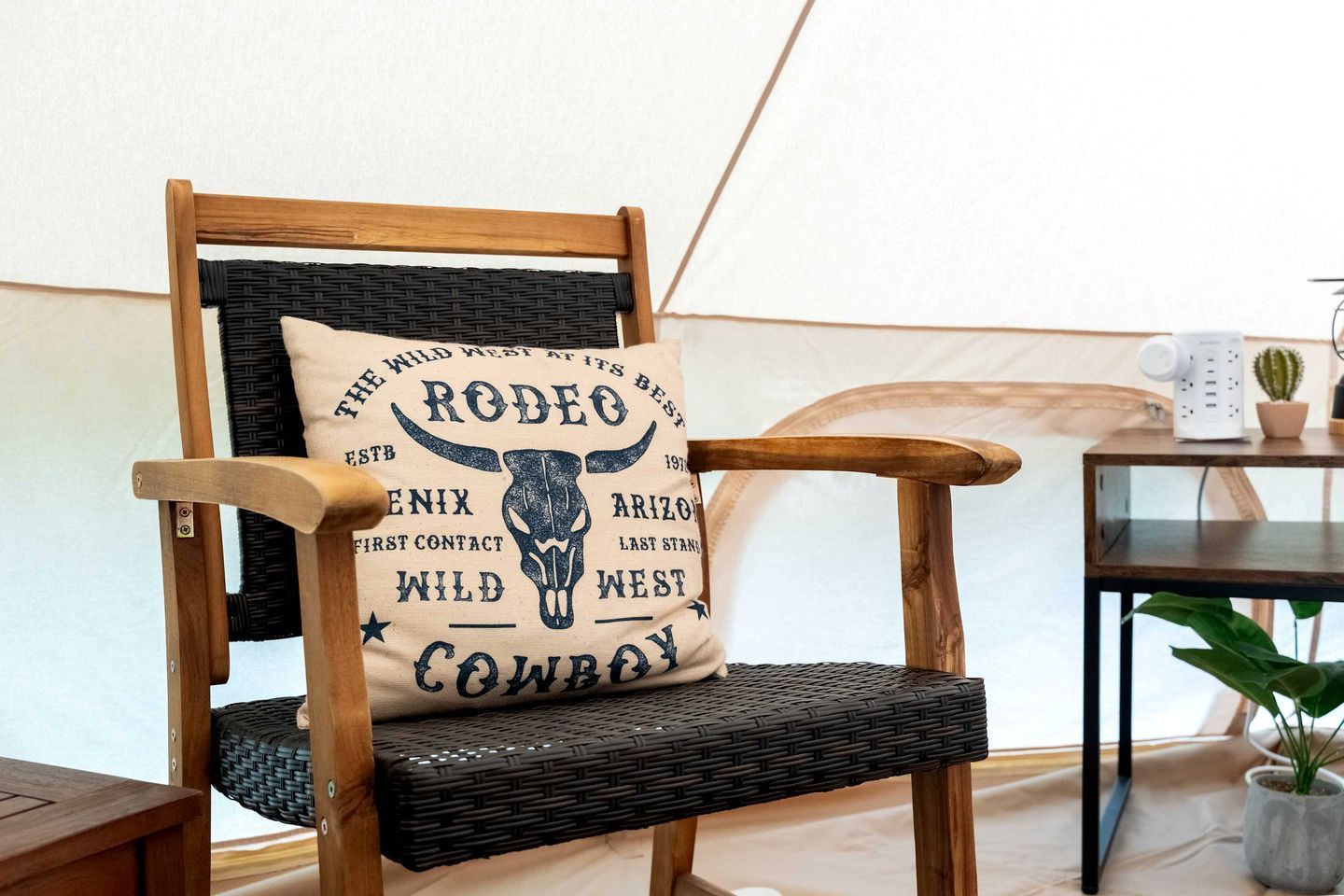 A rustic wooden chair with a black woven backrest and a pillow featuring a cowboy design.