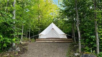 A white tent in a forested area with a gravel path leading to it.