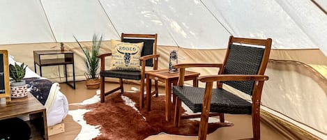A tent interior with a cowhide rug, wooden chairs, a small table, and a decorative pillow.