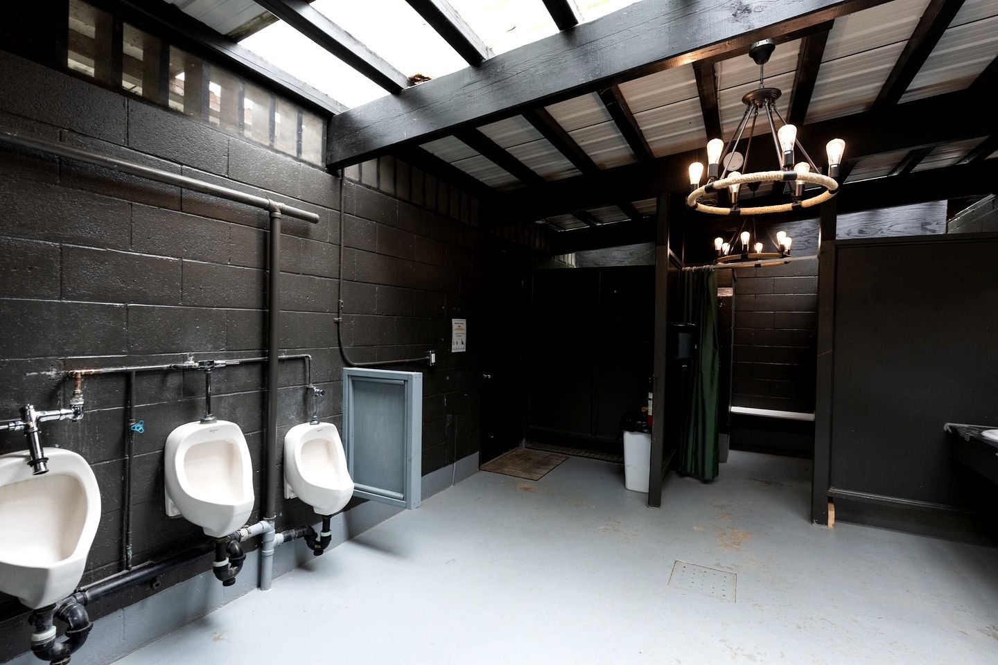 Baño de hombres con orinales, dispensador de toallas e iluminación colgante.