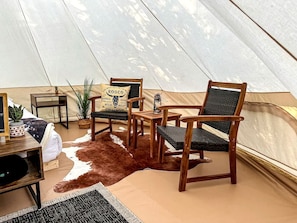 A tent interior with a cowhide rug, wooden chairs, a small table, and a decorative pillow.