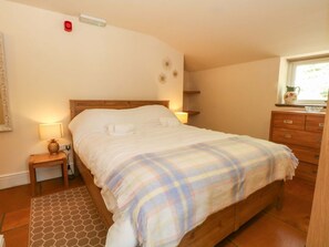 A bedroom with a bed, bedside table, lamp, dresser, and a window.