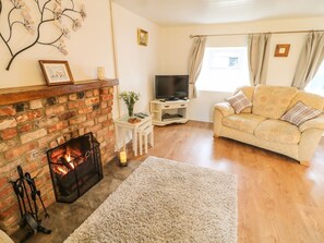 A living room with a fireplace, a sofa, a television, and a window with curtains.