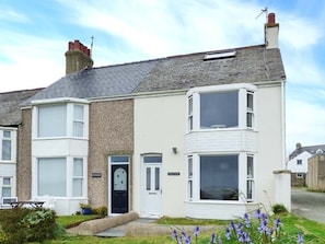 A two-story residential house with a white exterior, a black front door, and a small front yard with purple flowers. - Sandy Bank, Rhosneigr (Rhosneigr)