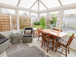 A conservatory with a dining table, chairs, wicker sofas, and a potted plant. - The Cottage, Marian-Glas (Marianglas)