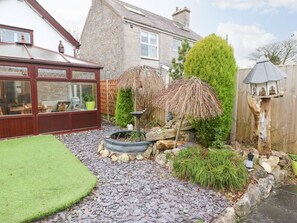 A garden with a patio, a wooden fence, and a birdhouse. - The Cottage, Marian-Glas (Marianglas)